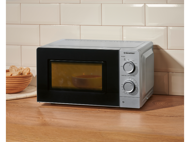 Silver microwave oven on a wooden countertop with a basket of bread slices.