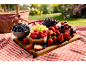 Fresh berries and grapes on a wooden board for a picnic on a red and white checkered blanket.