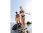 Man and woman in swimwear and water shoes walking on rocks by the sea.