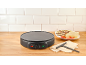 Electric crepe maker with banana and strawberry crepes on a wooden counter.