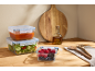 Glass food containers with salad, sauce, and berries on a wooden countertop