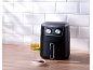 Black air fryer on a wooden counter with an oil jug and ketchup.