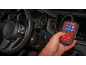Hand holding a car diagnostic tool with a screen displaying various functions inside a car.