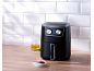 Black air fryer on a wooden counter with an oil jug and ketchup.