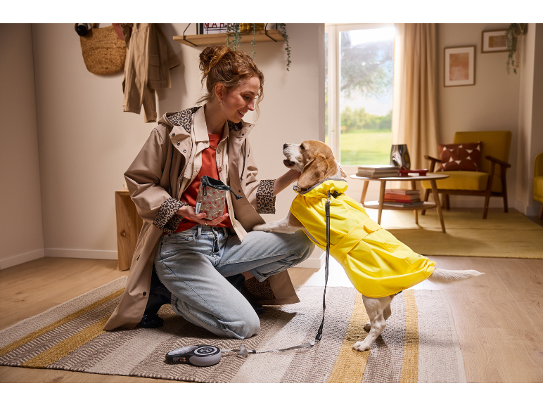 Woman with dog in yellow raincoat and treat bag, ready for a walk.