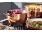 Copper pots with cooking vegetables and a pan with mushrooms on an induction hob.