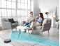 Robot vacuum cleaning a rug while a relaxed couple converses in a modern living room.