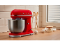 Red stand mixer with stainless steel bowl, eggs, and flour on a wooden countertop.