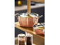 Copper pots and saucepans on a wooden shelf, with spices in the background.