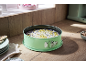 Green springform pan with cake on a wooden kitchen counter, with macarons in the background
