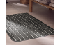 Grey striped bath mat on a tiled floor with folded towels in the background.