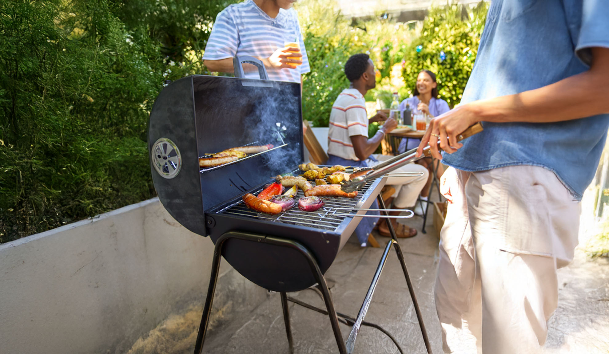 Friends enjoy a backyard barbecue grilling sausages and vegetables.