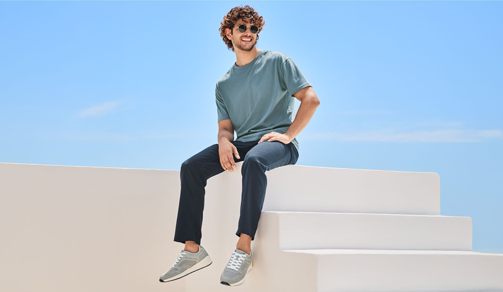 A man in a teal t-shirt and dark pants sits on white steps.