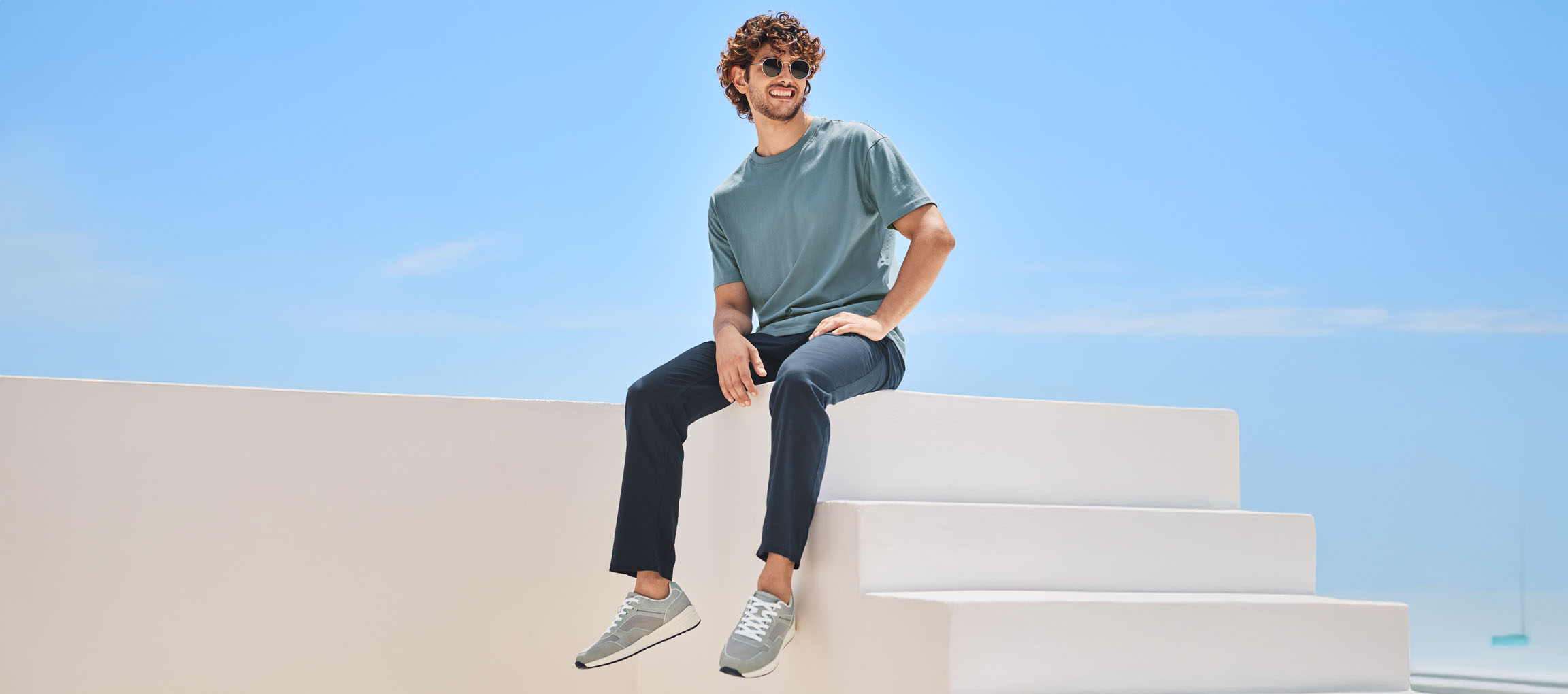 Man in a t-shirt, pants, and New Balance sneakers, sitting on white stairs.