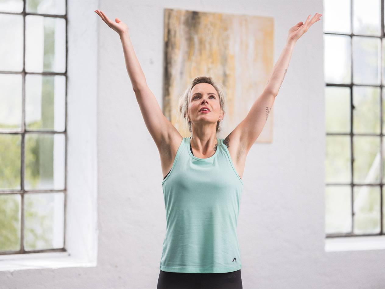 A woman in a teal athletic tank top with her arms raised.
