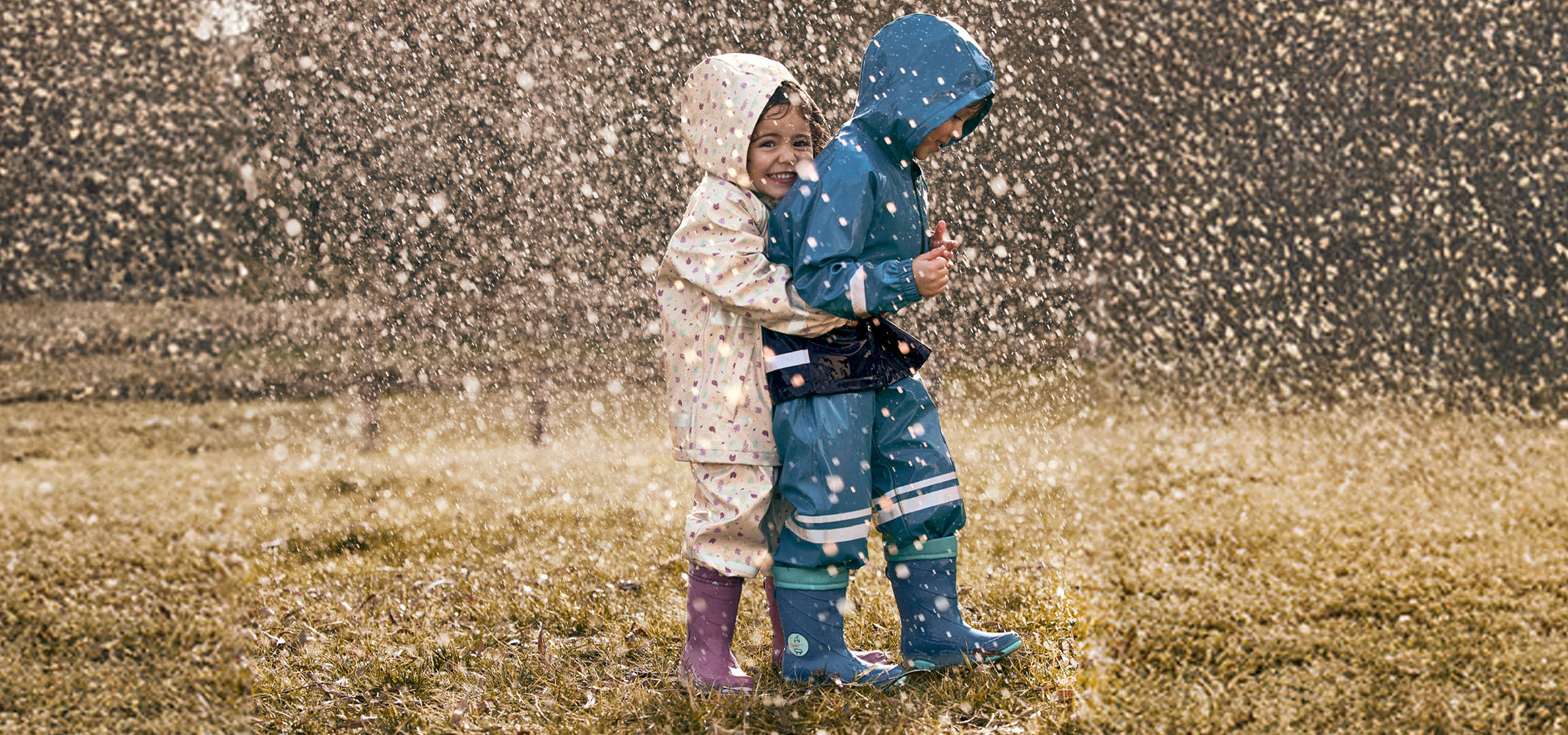 Two children in rain suits and rubber boots playing in the rain.