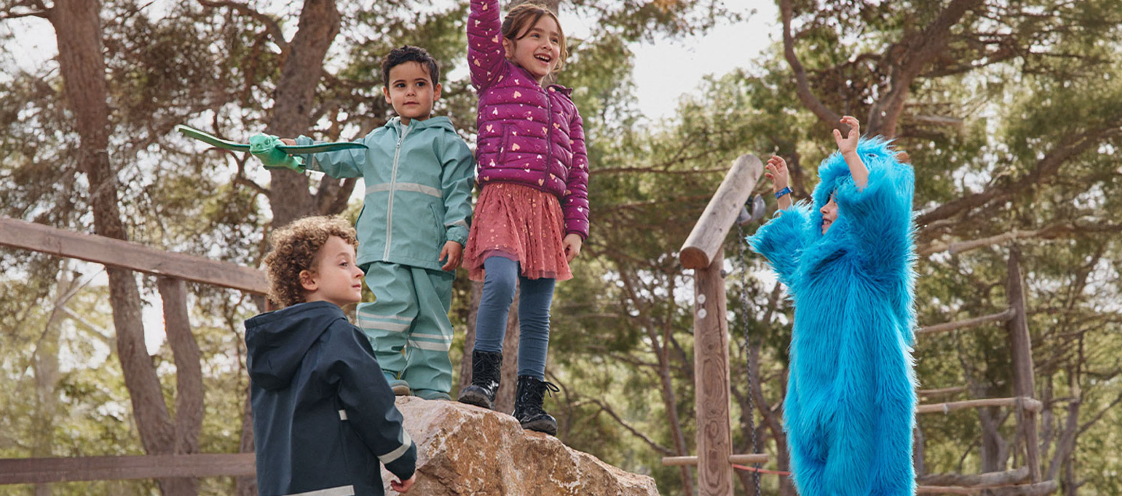 Four children playing outdoors, two in outerwear, one in a blue monster costume.
