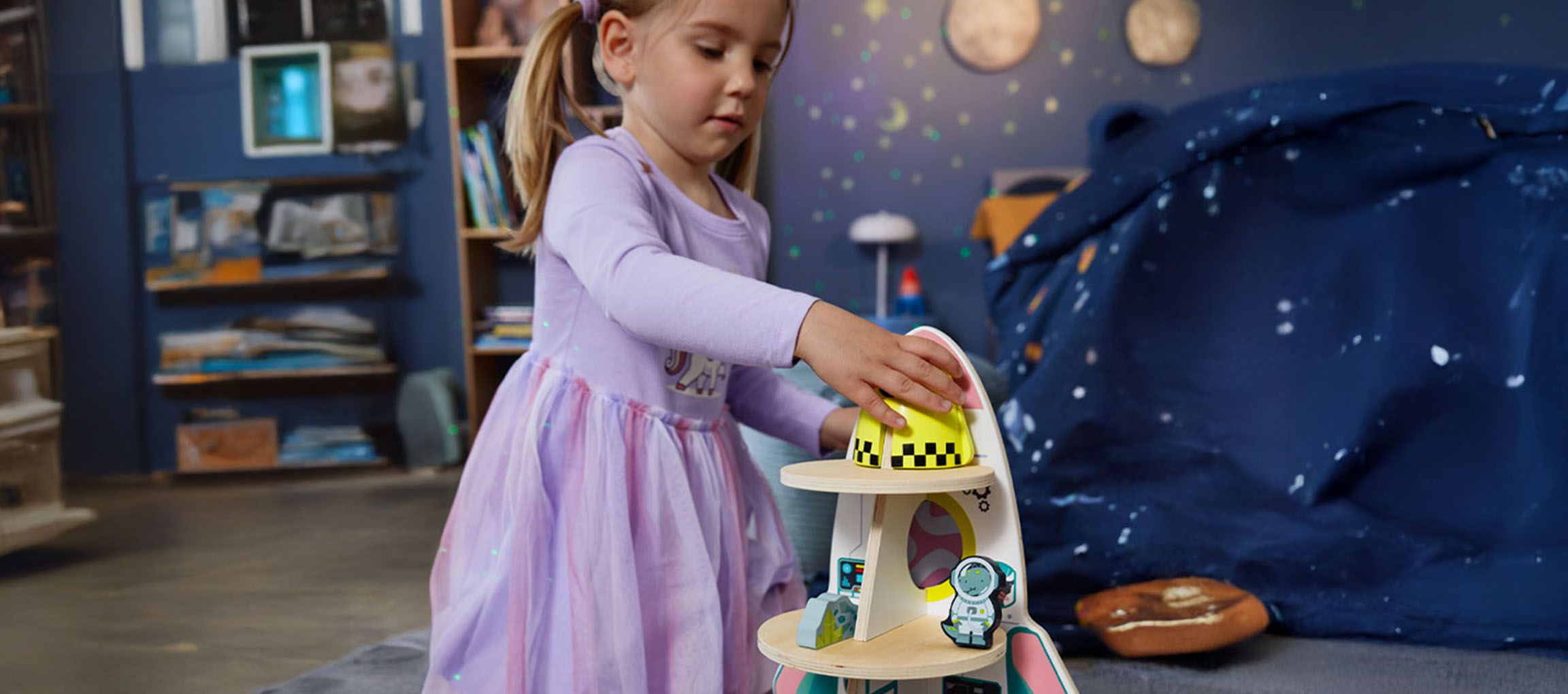 Little girl playing with a spaceship toy in a space-themed room.