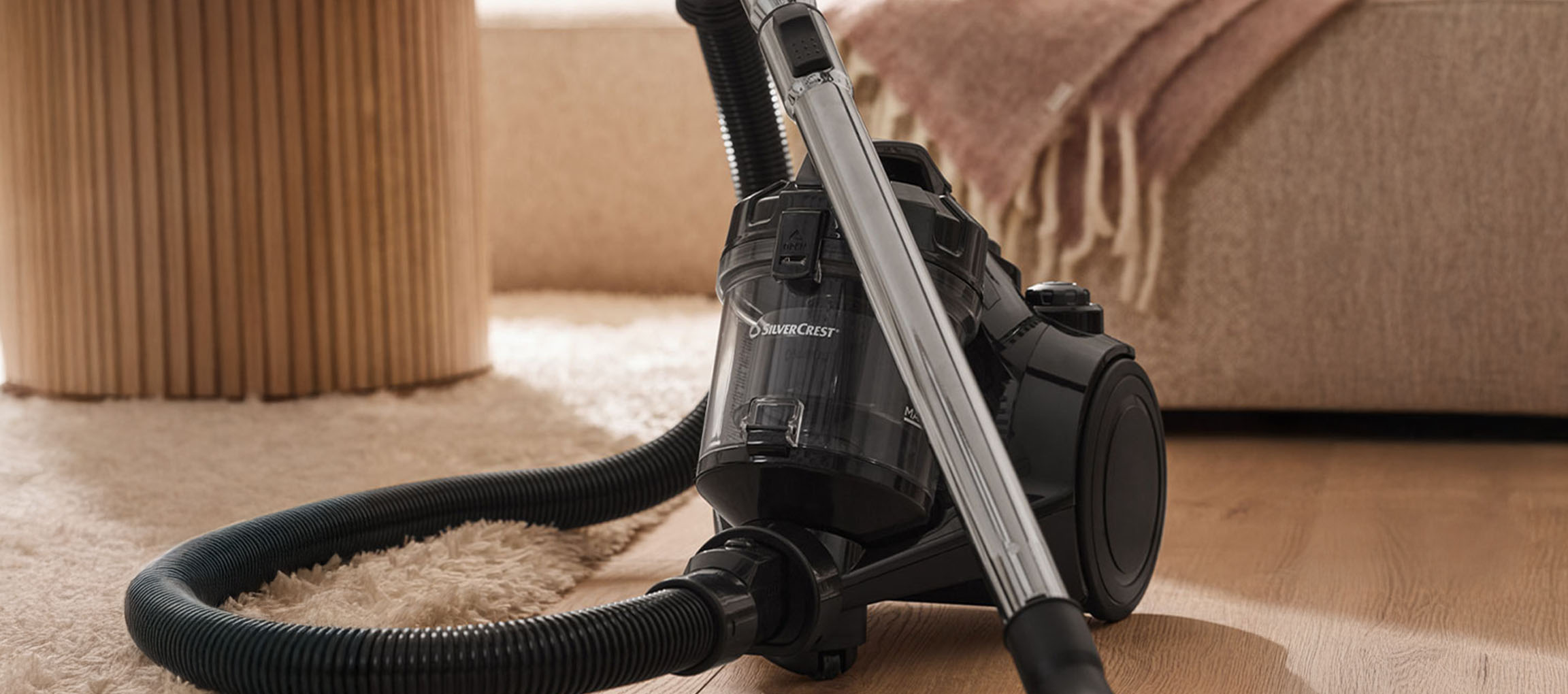 A black SilverCrest vacuum cleaner on a carpet and wooden floor.