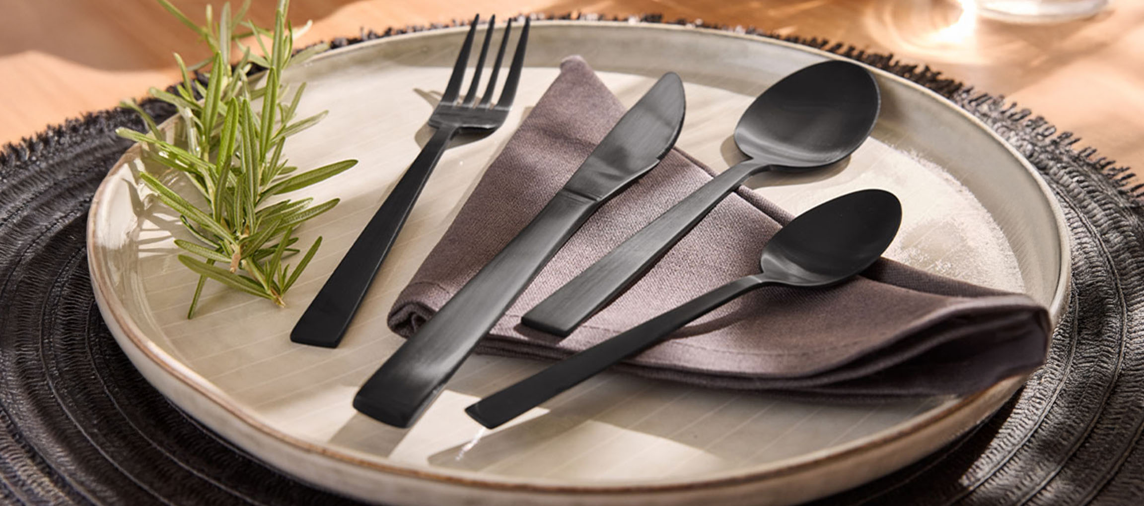 Matte black cutlery, plate, and napkin on a wooden table.