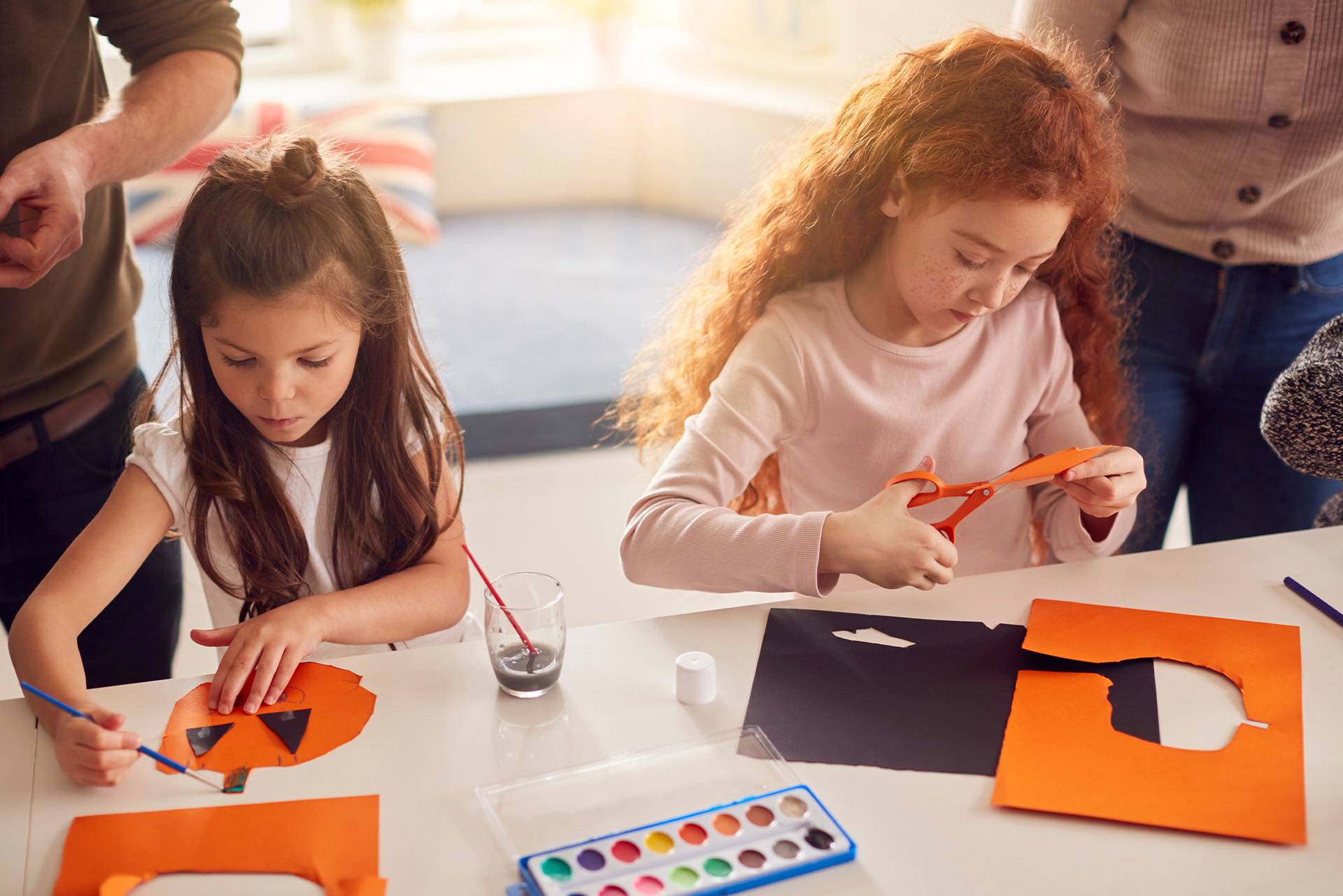 Two girls creating Halloween decorations from paper and paints.