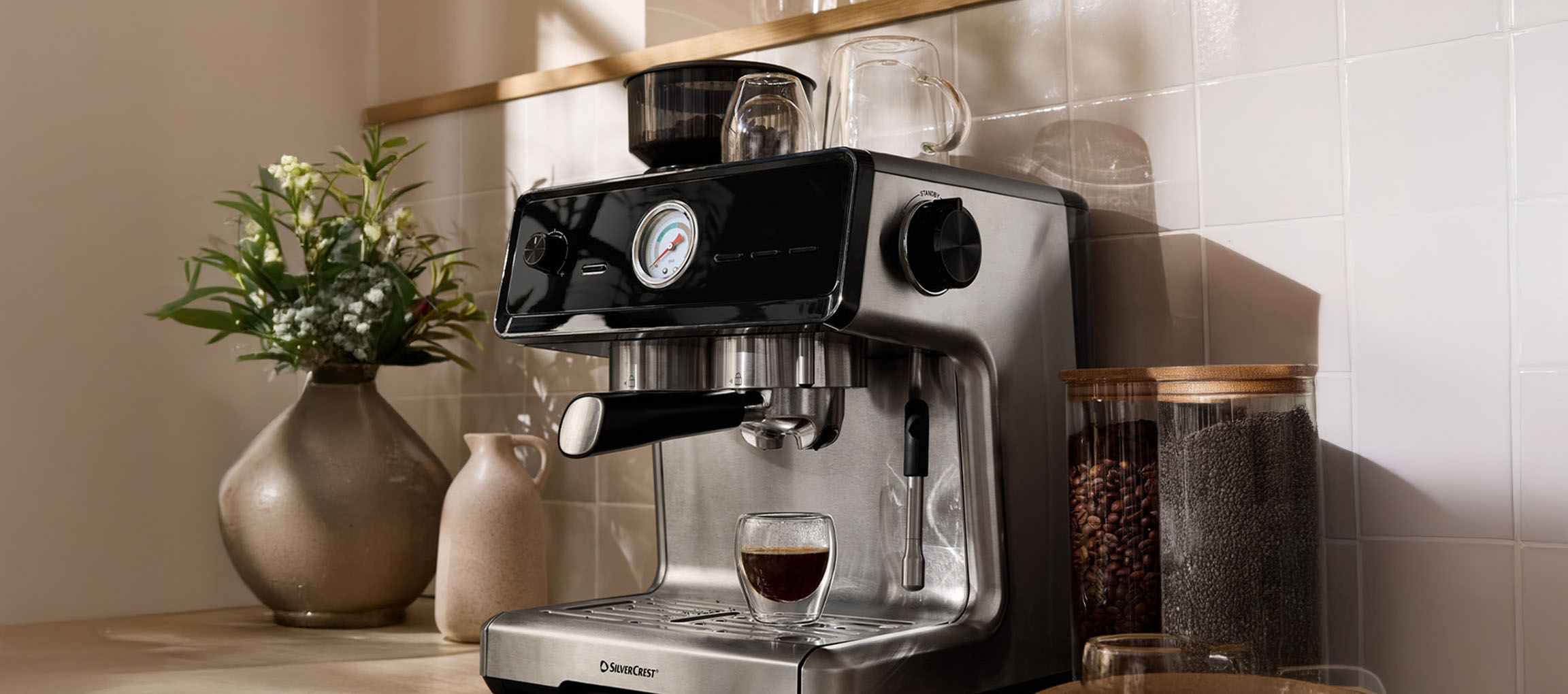 SilverCrest coffee machine on a kitchen counter, with a flower vase and jars.