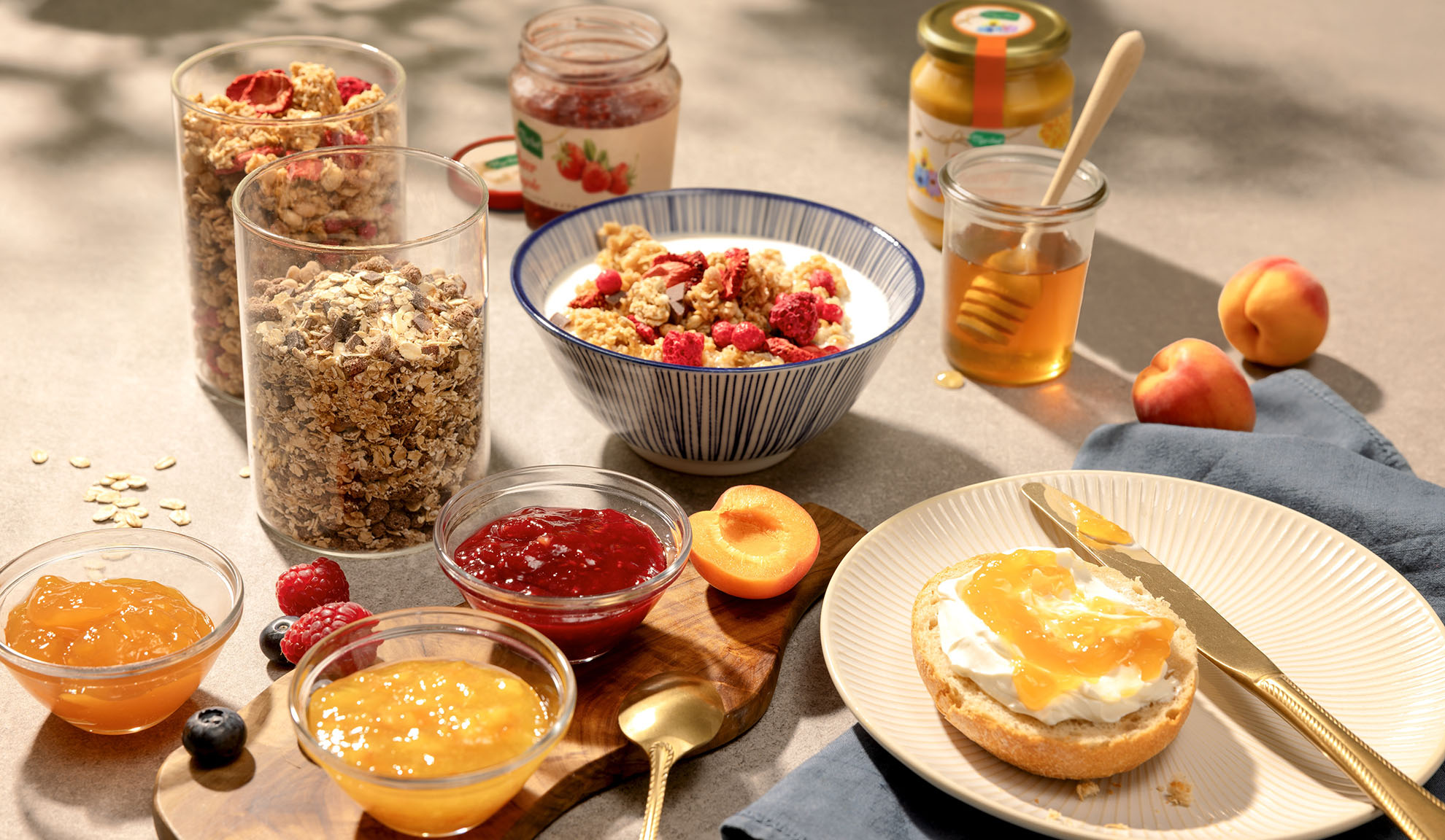 Breakfast spread with granola, yogurt, honey, jams, and fresh fruit on a sunlit table.