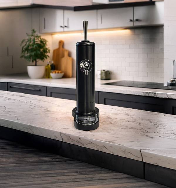 Black beverage dispenser on a marble kitchen counter with modern dark cabinetry.