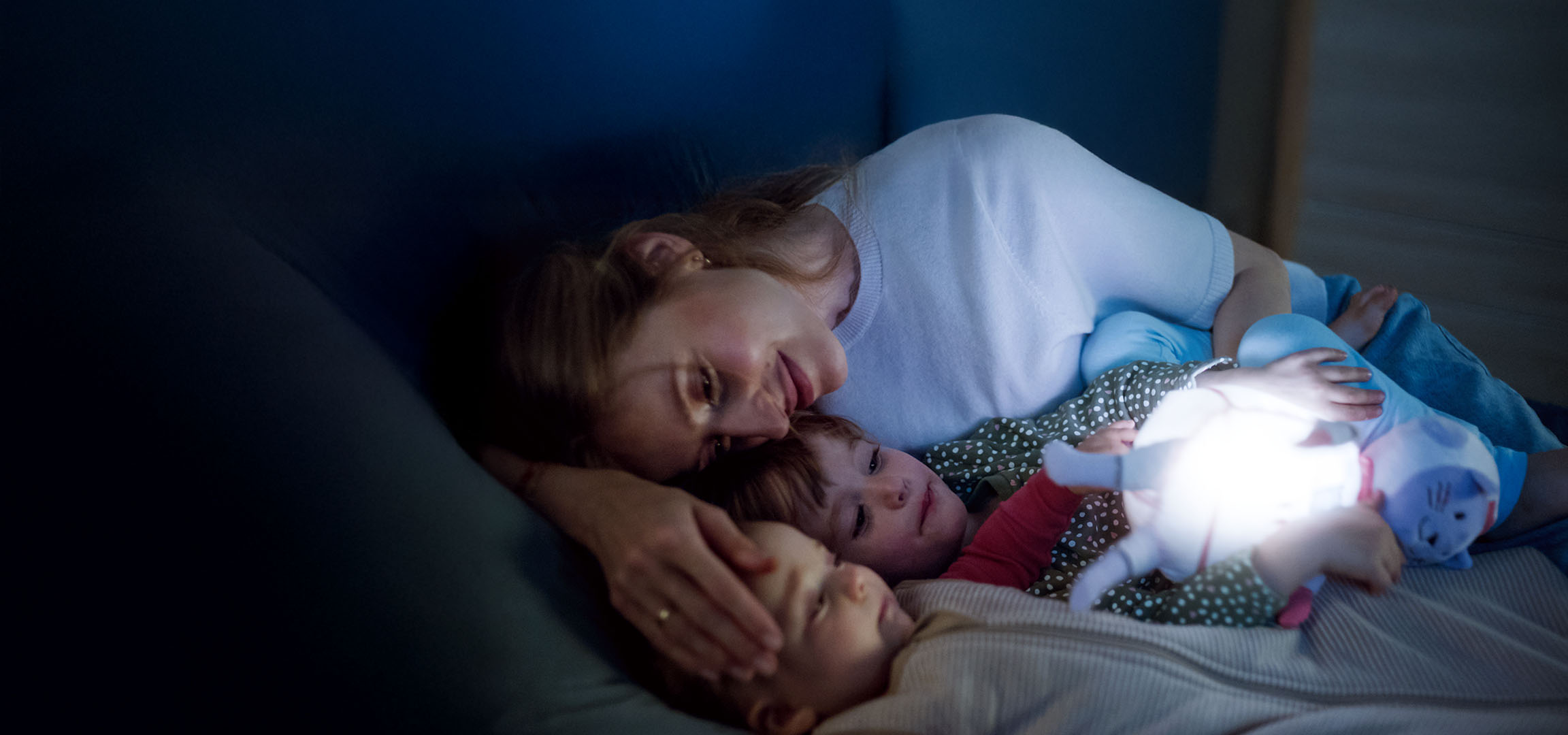 Mom and two children in bed with a glowing toy