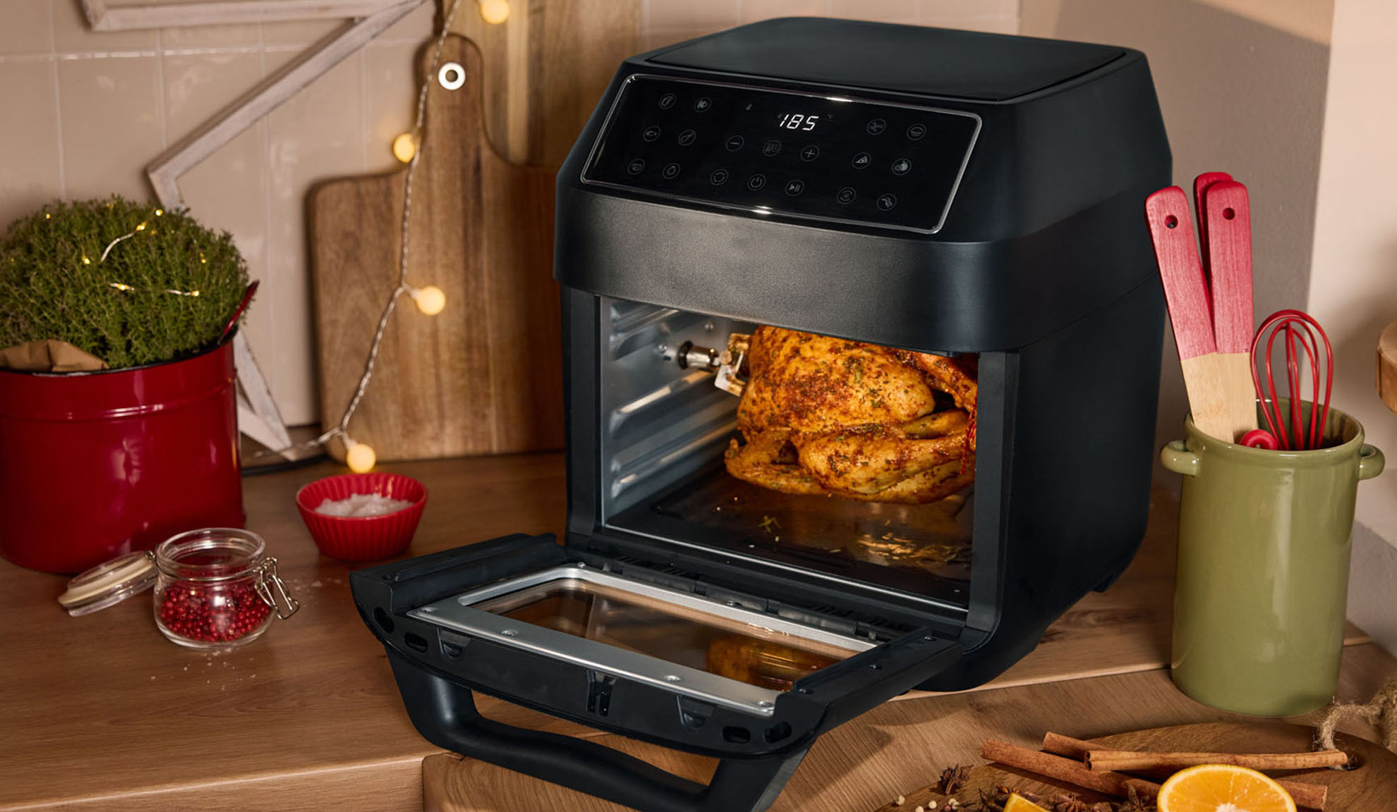 Air fryer with roasted chicken, spices, and Christmas decorations in the kitchen.