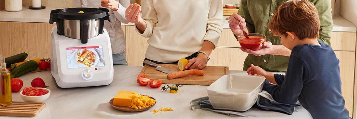 Family cooking with a food processor and other kitchenware.