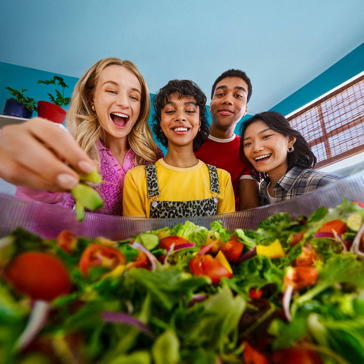 Four friends happily preparing a fresh salad with various vegetables.