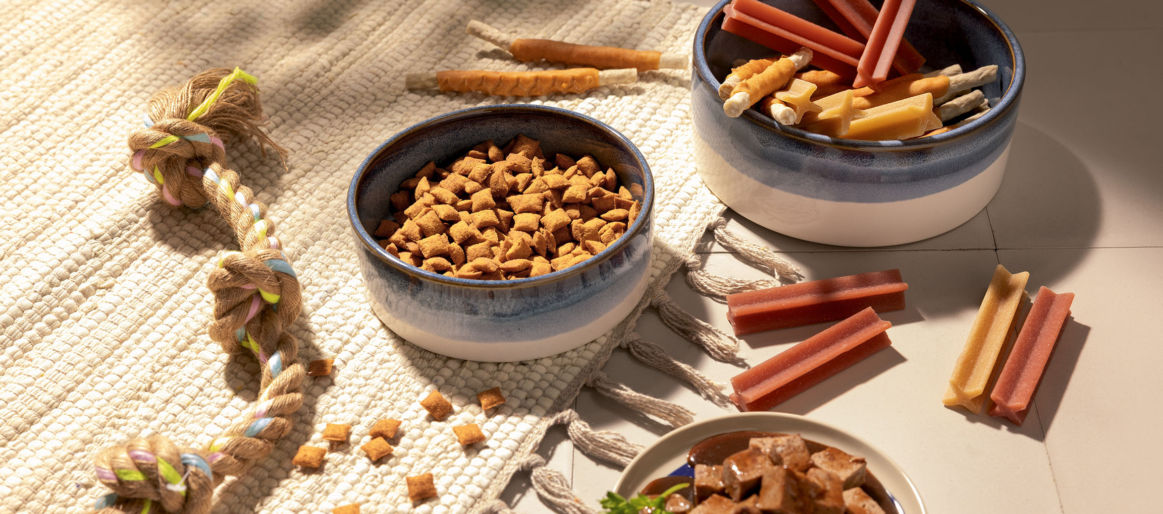 Assorted pet food and treats, including dry kibble, chew sticks, and a rope toy.