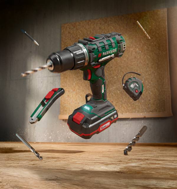 Cordless drill with battery, utility knife, tape measure, and drill bits floating in a workshop setting.