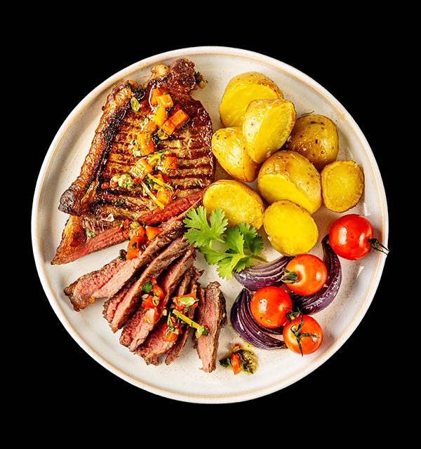 Grilled steak with roasted potatoes, cherry tomatoes, and red onion on a white plate.