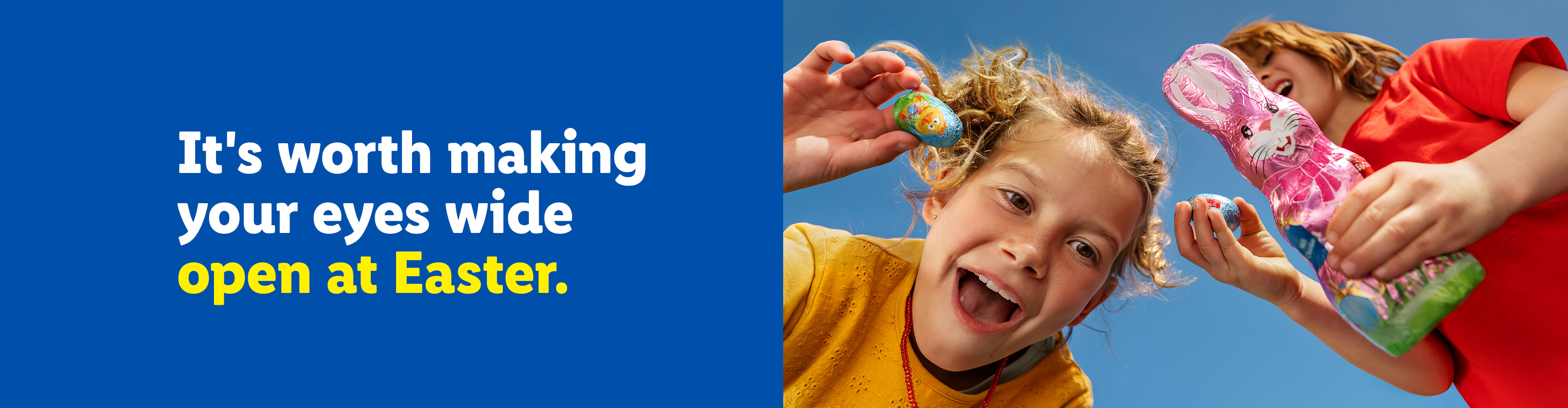Two happy children holding chocolate Easter eggs and a chocolate bunny against a blue sky.