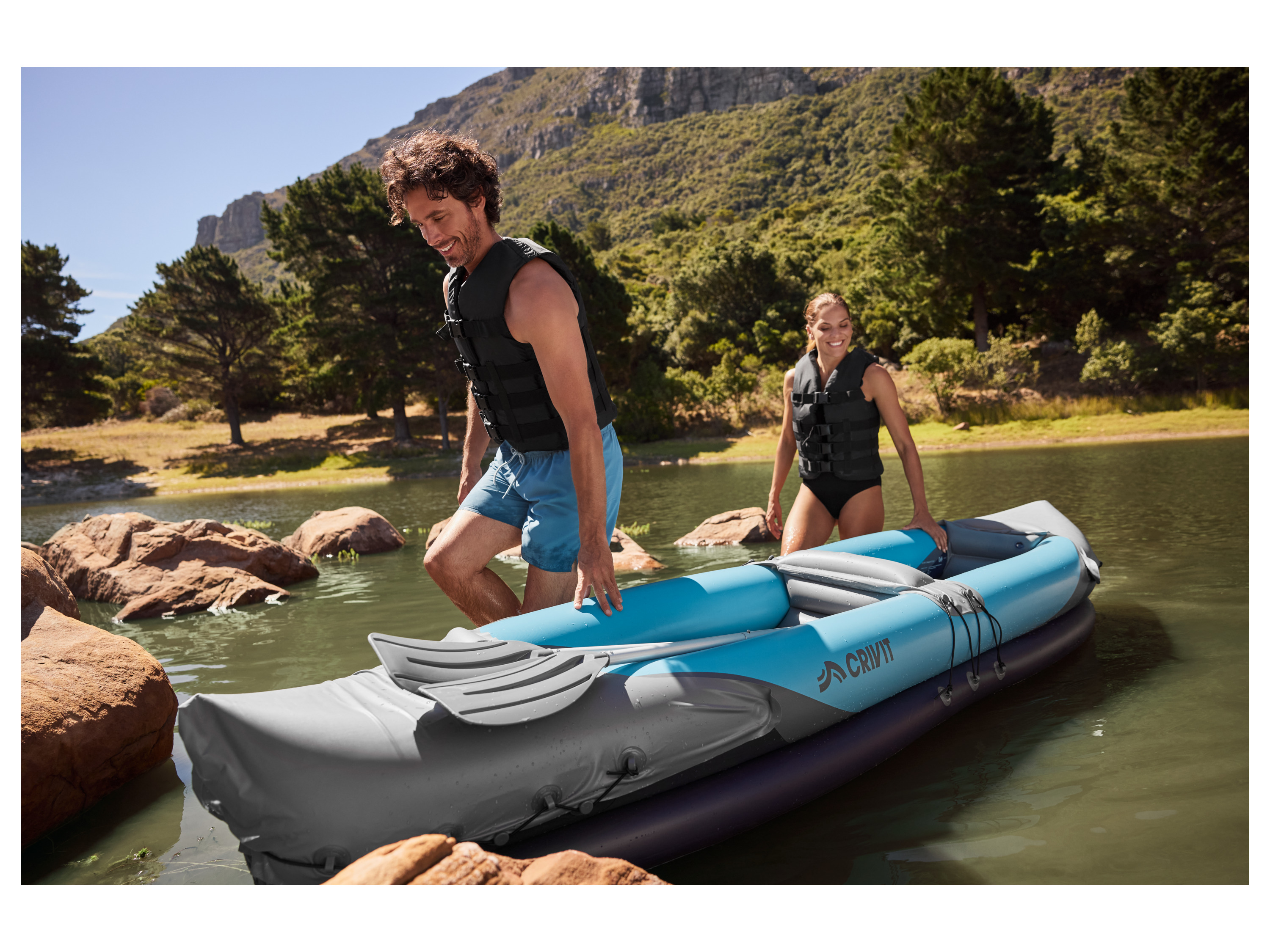 A couple prepares to kayak on a calm lake, using a CRIVIT inflatable kayak.