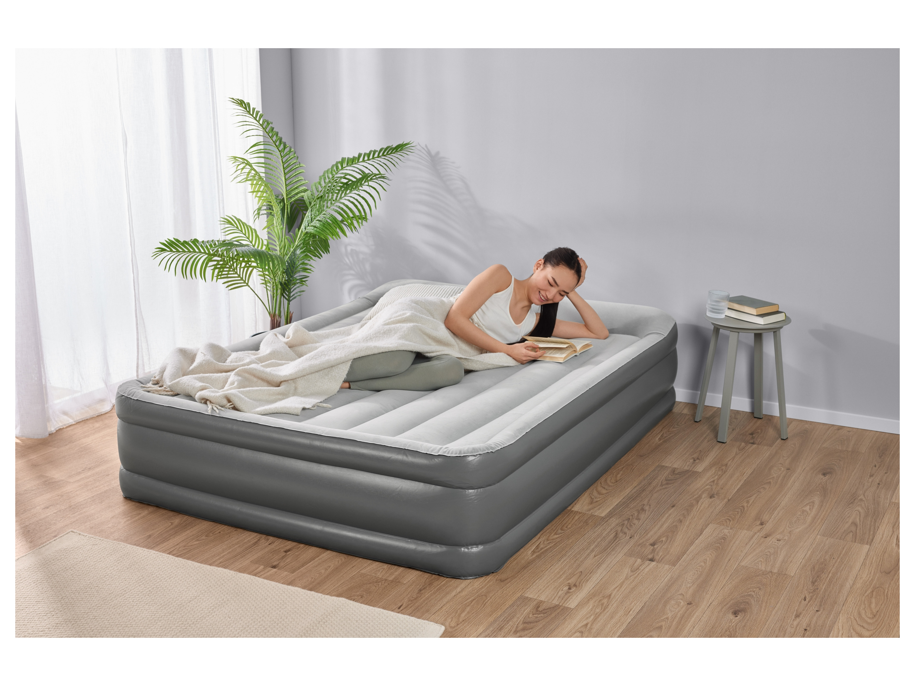 A woman relaxes on a gray Intex inflatable air mattress while reading a book.