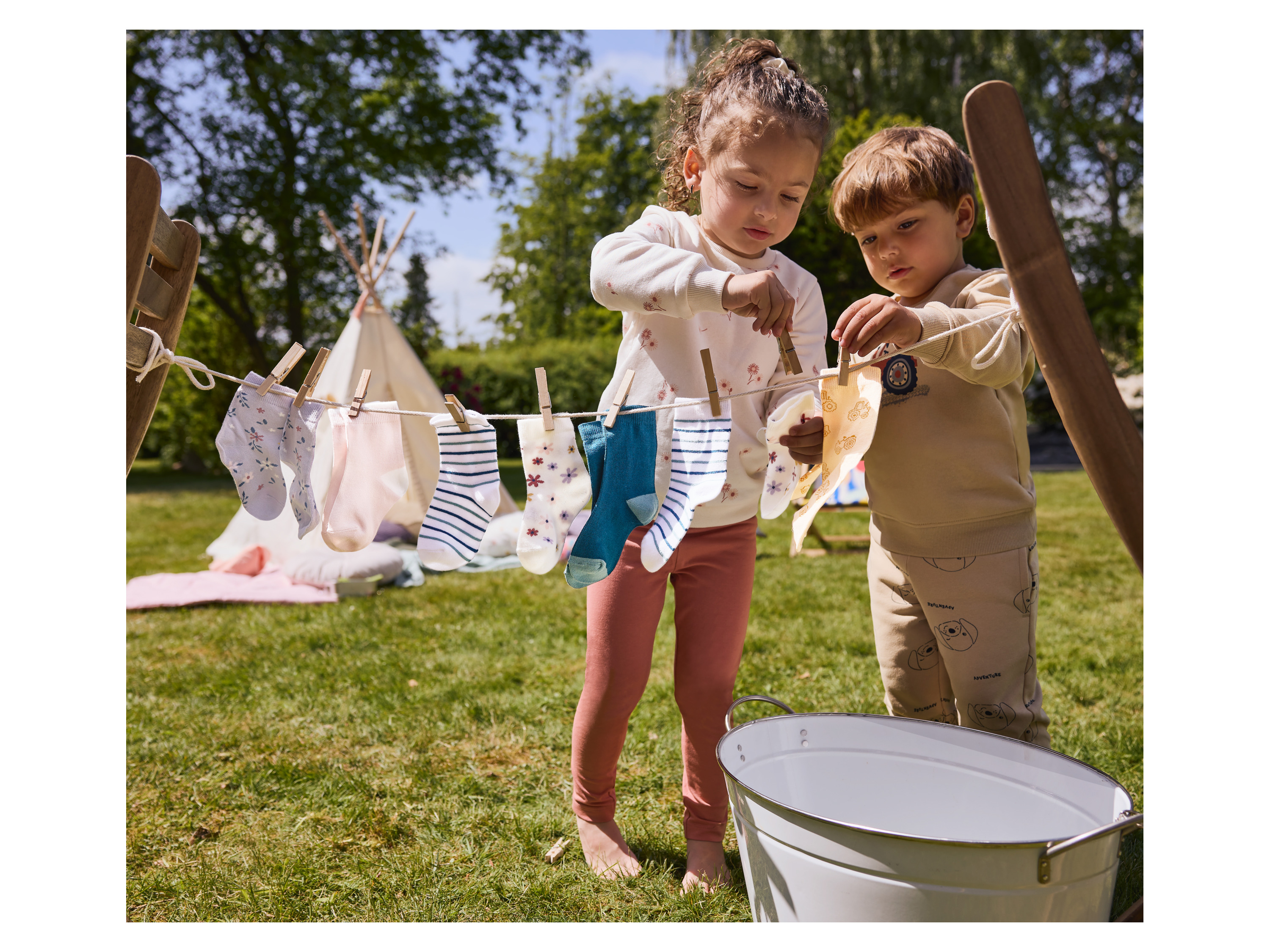 Two children hanging socks on a clothesline in a garden.
