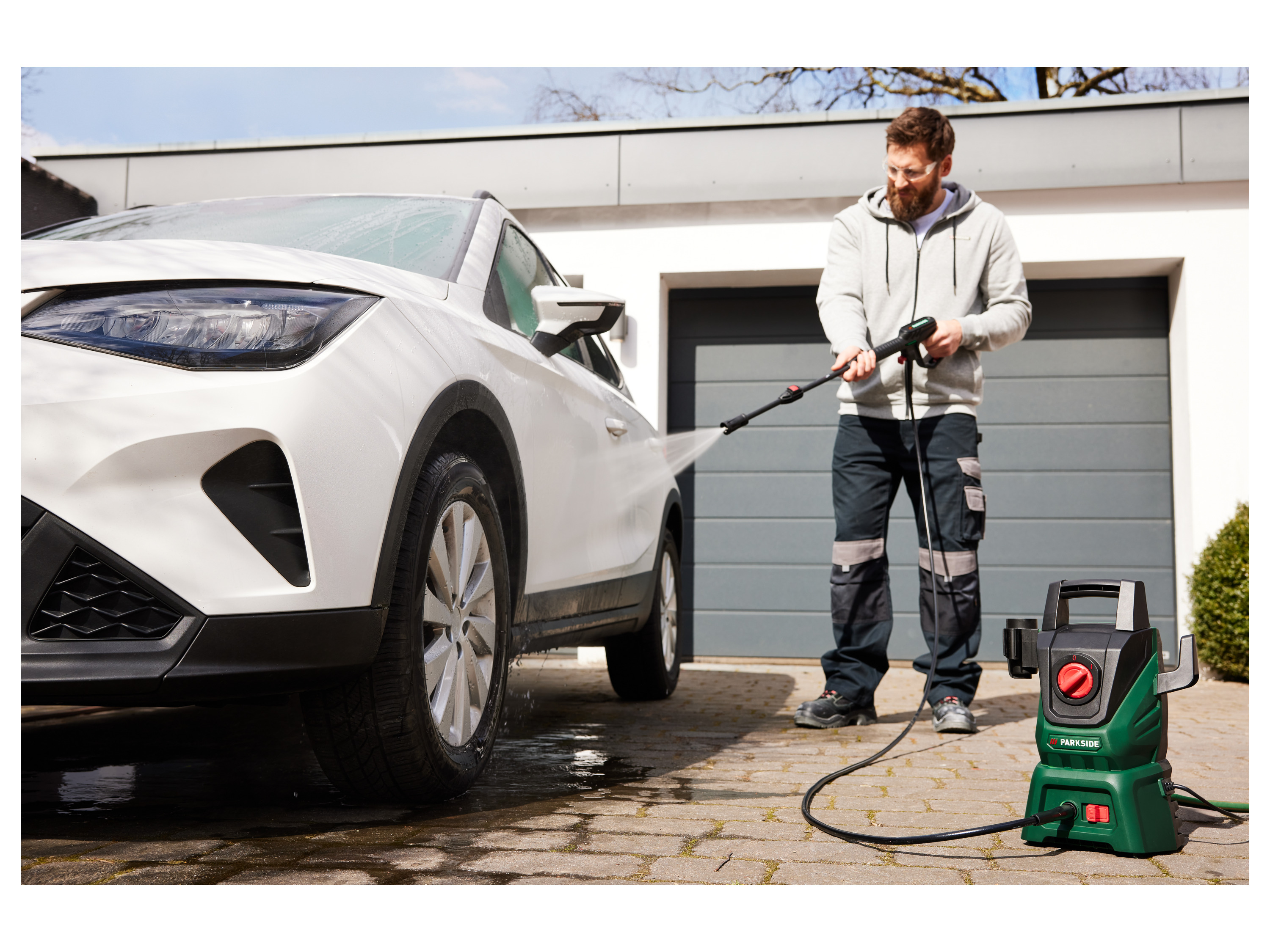 A man uses a Parkside pressure washer to clean his white car.