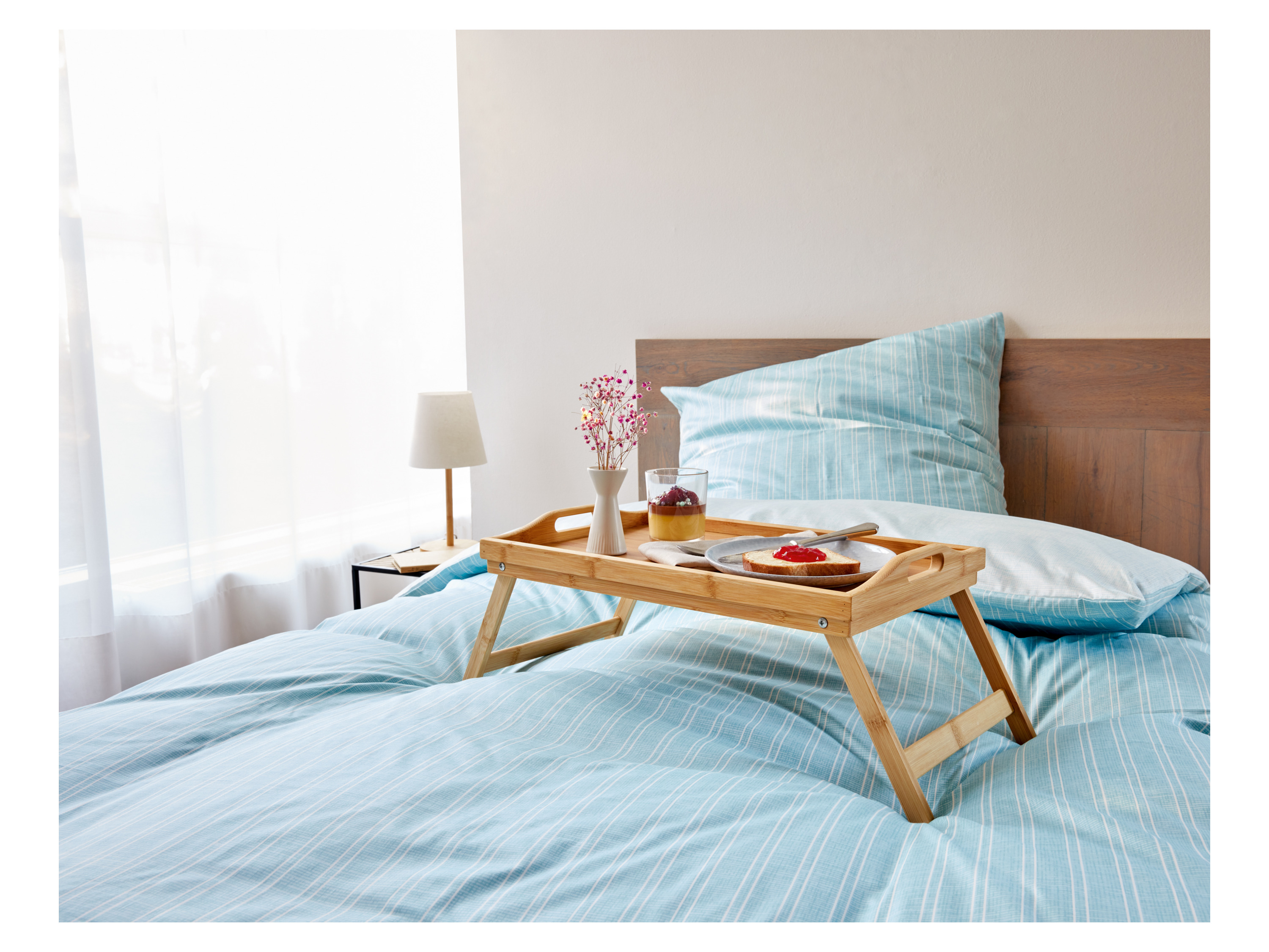 Breakfast in bed with a wooden tray, a slice of cake, and a glass of dessert.