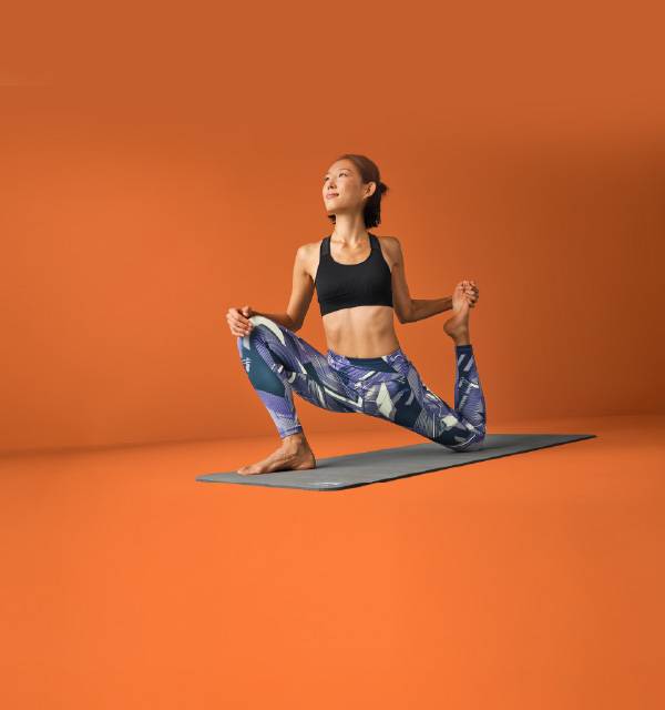 Woman in black sports bra and patterned leggings doing yoga on a mat.