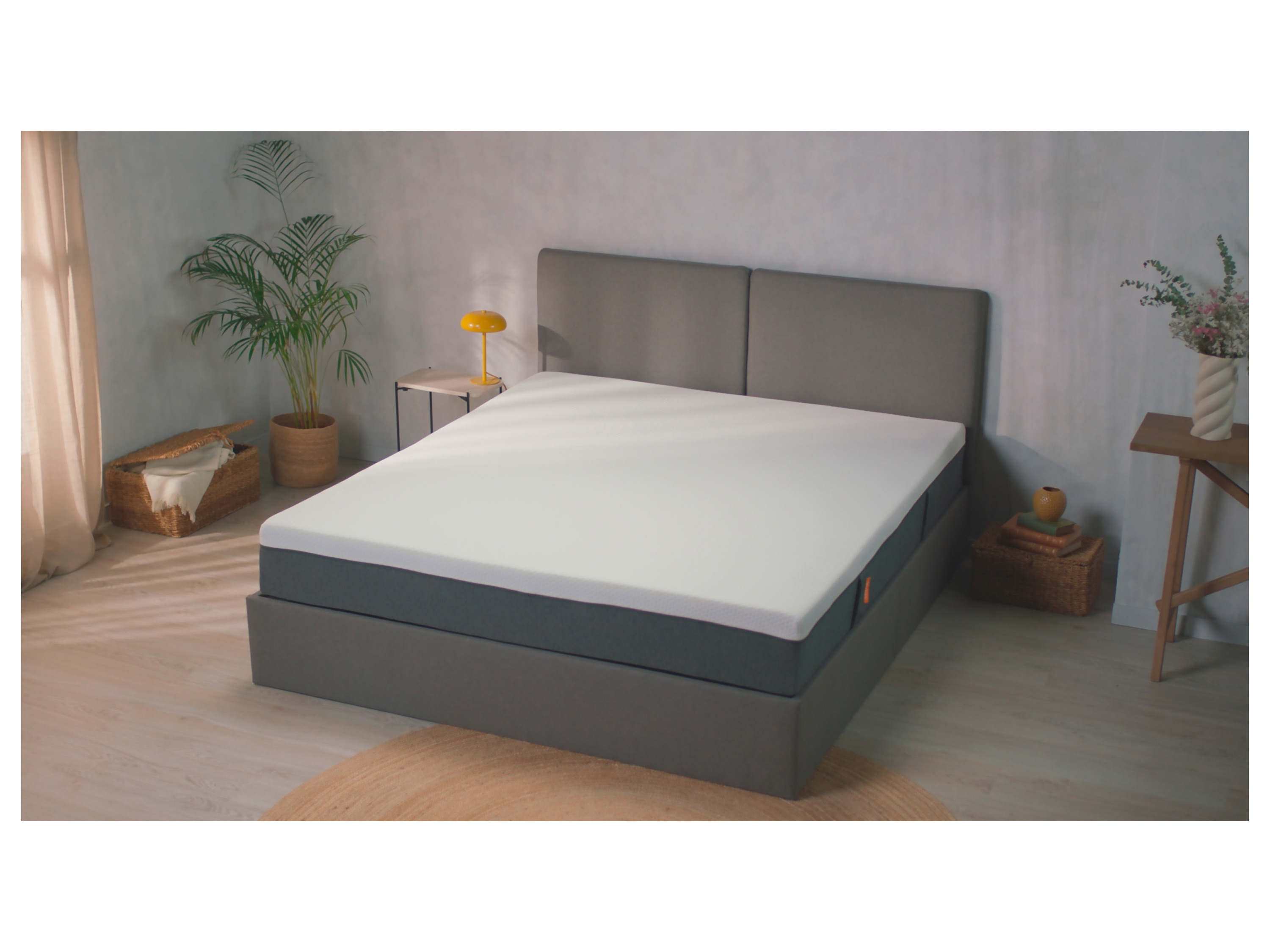 A gray upholstered bed frame with a white mattress sits in a minimalist bedroom.