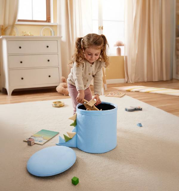 Child playing with a blue dinosaur toy storage box and wooden toys on a rug.