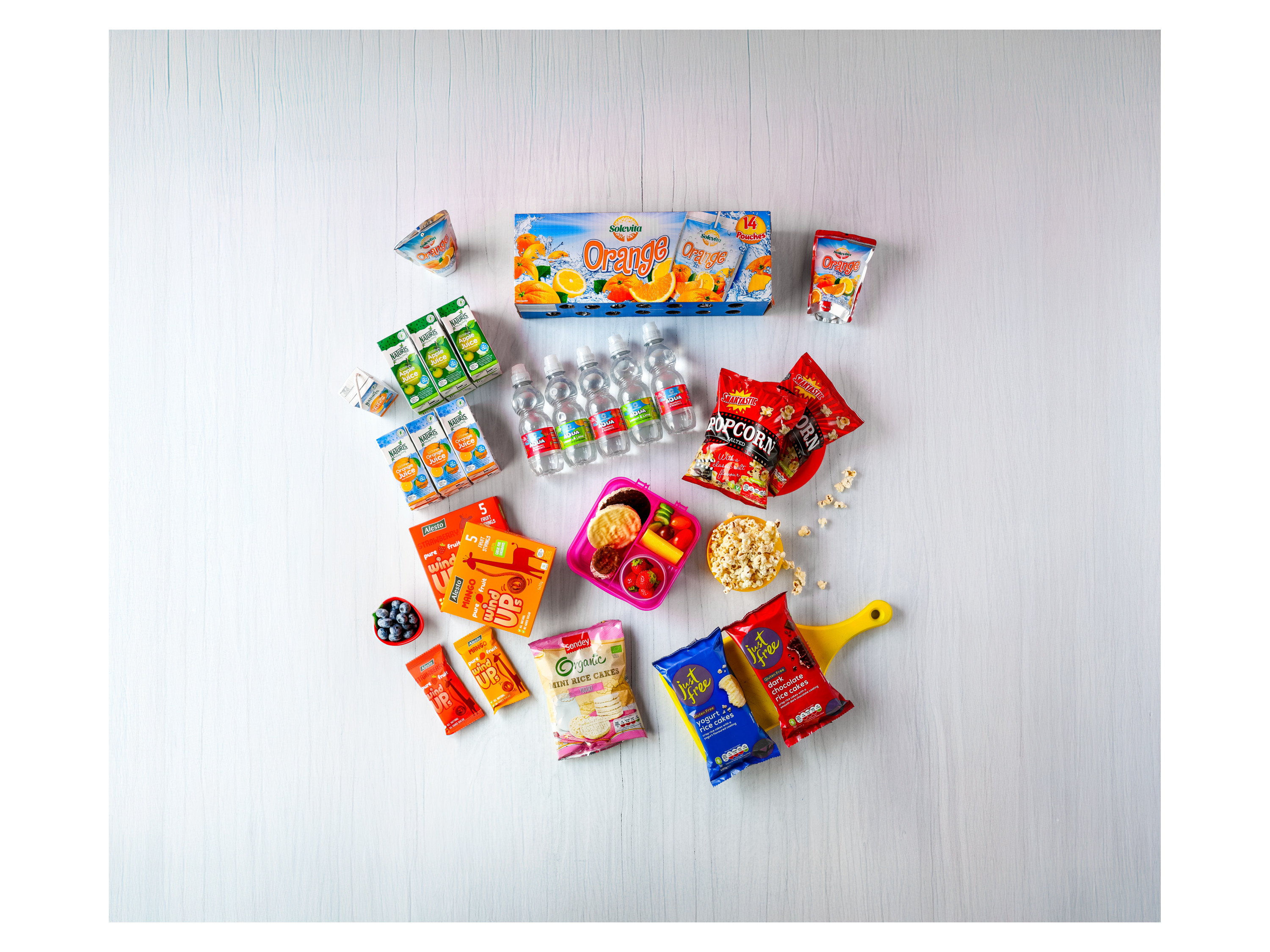 A variety of snacks and drinks, including juices, water, popcorn, fruit snacks, and rice cakes.