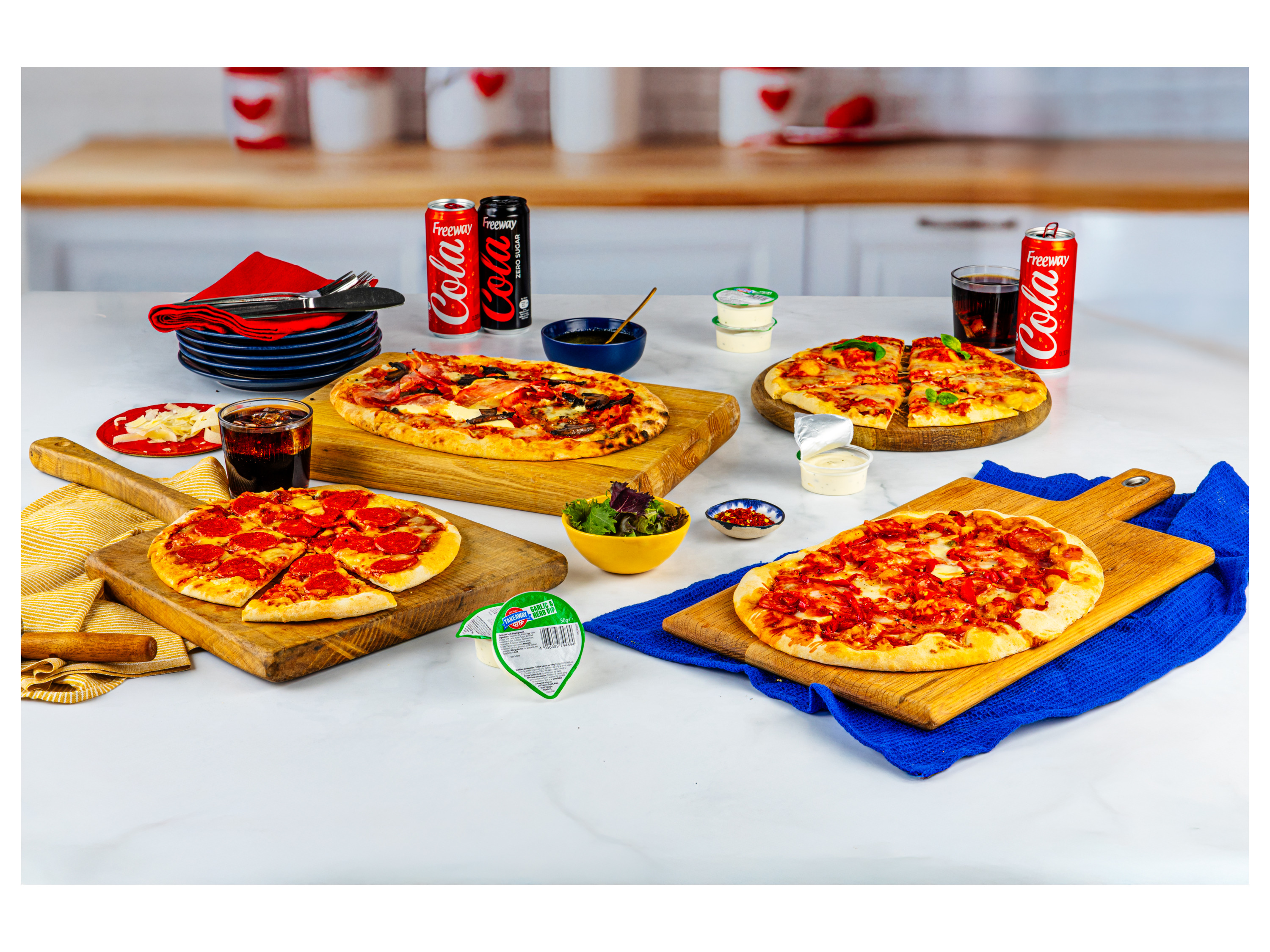 Four delicious pizzas and Freeway Cola cans are arranged on a kitchen counter.