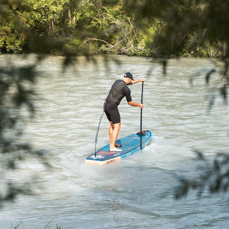 Man in wetsuit and life vest paddling a blue paddleboard on a river.