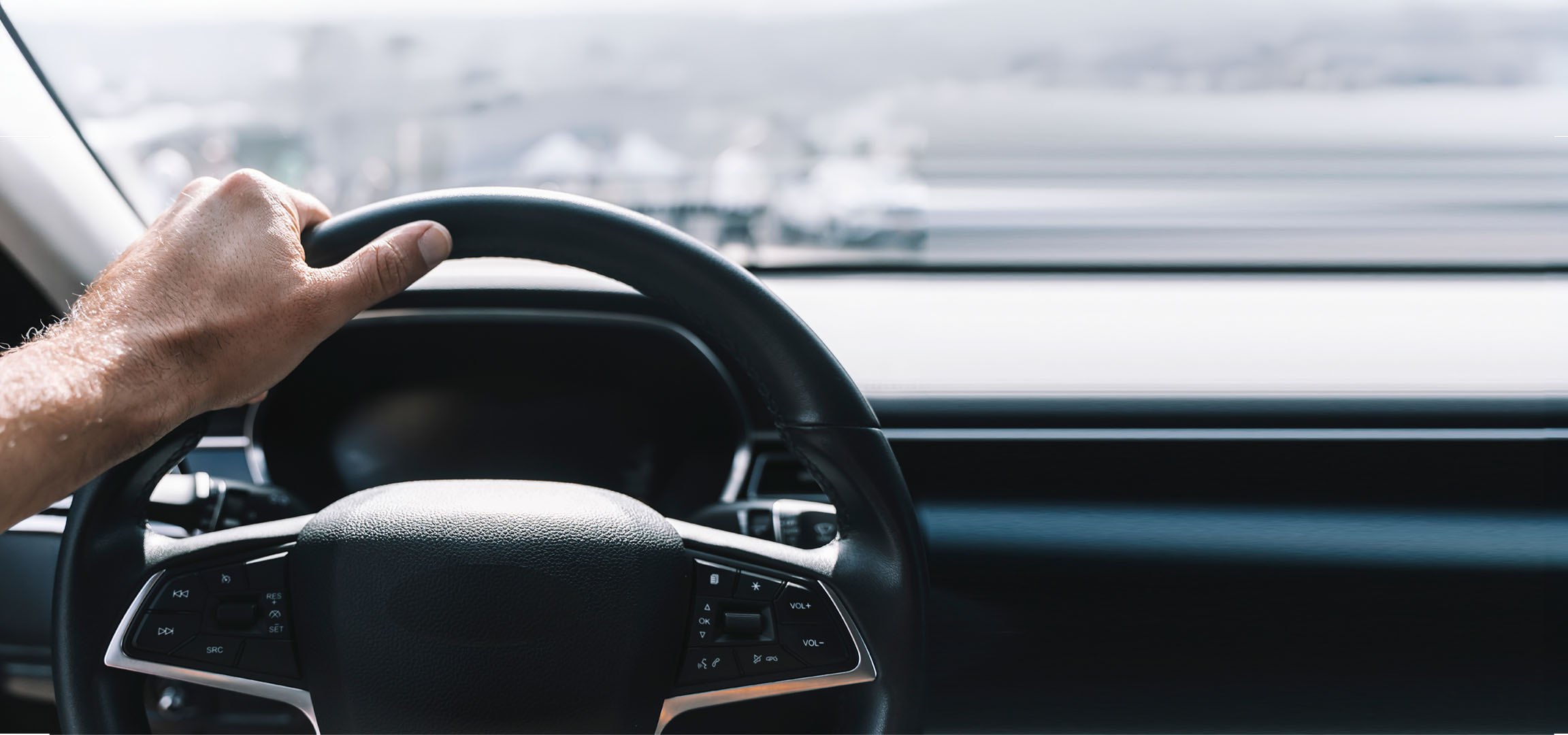 Man's hand holding a car steering wheel.
