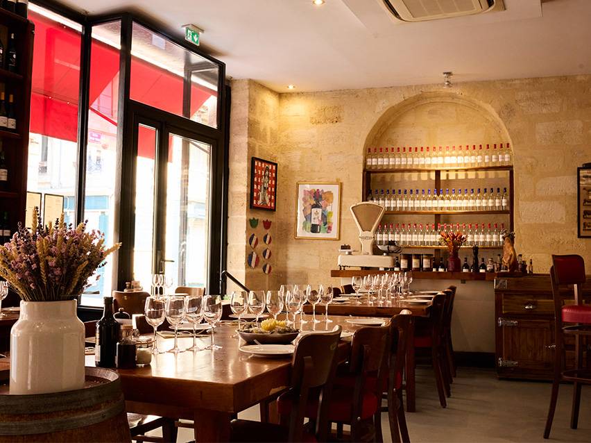 Restaurant interior with wooden tables, wine bottles on shelves, and a large window.