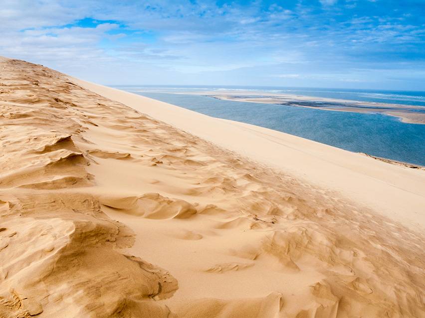Golden sand dune with a blue lagoon and cloudy sky in the background.